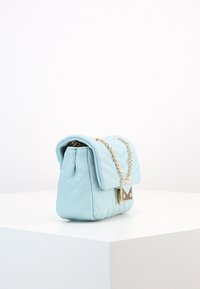 Světle modrá prošívaná kabelka s řetízkovým popruhem a kovovým zapínáním, s pevnou, obdélníkovou siluetou a hladkým povrchem.