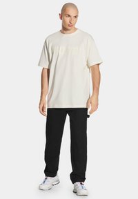 Jasna kremowa, luźna koszulka z delikatną grafiką, w zestawieniu z luźnymi czarnymi spodniami i białymi trampkami z wielokolorowymi akcentami.