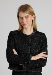 Schwarze strukturierte Jacke mit einem cropped Design, rundem Ausschnitt und Knopfverschluss. Verziert mit Akzenten entlang des Kragens und der Ärmelbündchen.