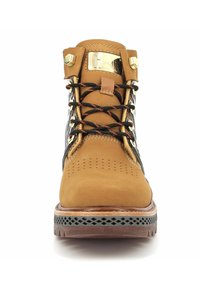 Bota de senderismo de piel marrón con acentos negros, herrajes dorados y cordones naranjas. Parte superior texturizada con perforaciones y suela robusta.