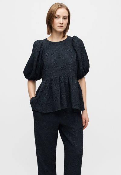 Top peplum bleumarin închis cu model floral texturat, mâneci scurte cu volum și croială lejeră. Asortat cu pantaloni bleumarin închis asortați.