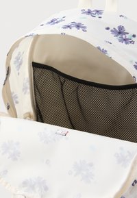 Λουλουδάτο σακίδιο πλάτης σε κρεμ απόχρωση με μωβ λουλούδια. Το εσωτερικό διαθέτει θήκη από δίχτυ και απαλή, ελαφριά ύφανση. Το επάνω καπάκι καλύπτει τον κύριο χώρο.