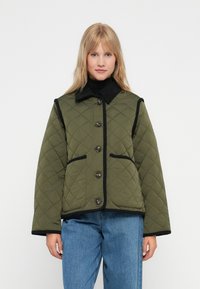Quiltet olivengrøn jakke med sort kant, der har en krave, fortil knapper og to sidelommer. Glat tekstur, afslappet design.