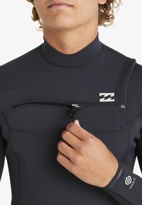 Traje de neopreno negro con cuello alto, textura suave y un bolsillo con cremallera en la parte delantera. Presenta un logo de la marca y costuras selladas para mayor durabilidad.