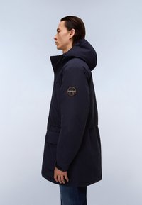 Námorní parka s kapucí, featuring nášivku na rukávu, přední kapsy a mírně zúžený pas. Hladká textura a utilitární design.