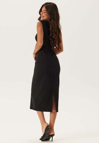 Svart ärmlös midiklänning med figurnära livstycke, sidoklyfta och slät textur. Bärs med svarta klackskor.