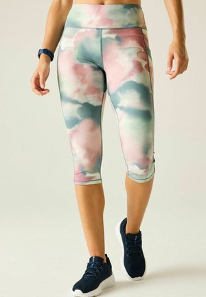 Benenen die hooggetailleerde, tie-dye capri leggings dragen in roze, groen en wit, gecombineerd met zwarte sportschoenen en een blauw fitnesshorloge.