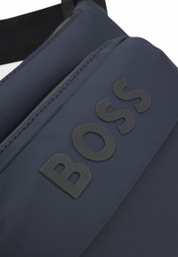Borsa a tracolla blu navy realizzata in tessuto testurizzato con logo "BOSS" in gomma nera. Caratterizzata da un scomparto con cerniera e tracolla regolabile.