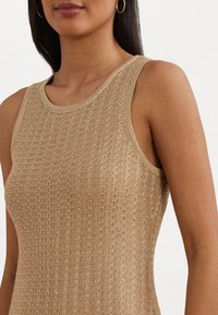 Top sin mangas de punto beige con un patrón texturizado, que presenta un escote y sisas acanalados, mostrando una silueta ajustada.