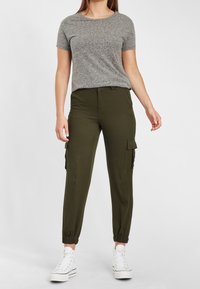 Šedé kratší tričko s krátkým rukávem v kombinaci s olivovými cargo kalhotami s bočními kapsami a elastickými manžetami, doplněné bílými vysokými teniskami.