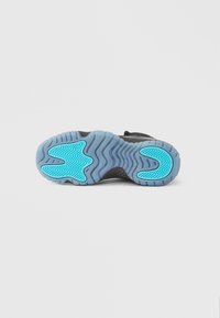 Μαύρη σόλα αθλητικού παπουτσιού με κυματιστή υφή, διαθέτει ανοιχτό μπλε διακοσμητικό σχέδιο. Κατασκευασμένη από καουτσούκ, σχεδιασμένη για πρόσφυση και ανθεκτικότητα.