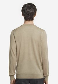 Beige långärmad tröja med rund halsringning, slät textur och ribbade manschetter och nederkant, bärs av en modell sett bakifrån.