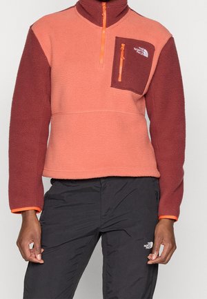 Osoba nosząca dwukolorowy polar z kieszenią na piersi oraz czarne spodnie, obie rzeczy z logo The North Face.