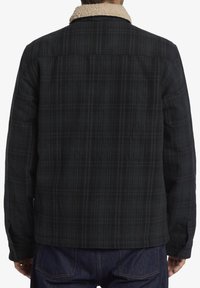 Black plaid jacket with a beige sherpa collar, featuring a straight cut and long sleeves. Textured fabric with a subtle check pattern.
