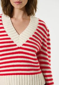 Maglione a righe rosse e bianche con scollatura a V, dotato di polsini e orlo a costine. Il tessuto sembra morbido con una finitura texturizzata.