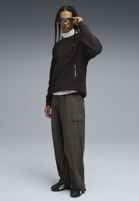 Felpa nera oversize con tasca con zip, pantaloni cargo grigi con tasche laterali a pattina e scarpe sportive nere. Modella con occhiali da sole riflettenti.