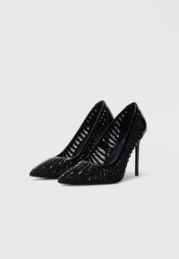 Décolleté nere con tacco alto a punta, caratterizzate da un motivo intrecciato e una superficie liscia, montate su sottili tacchi a spillo.