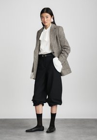 Sivý sako s rybej kostí, biela blúzka s mašličkou, čierne skrátené nohavice a elegantné čierne baleríny. Výrazné veľké náušnice a čierne ponožky.