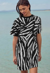 Robe à manches courtes noir et blanc à rayures avec une coupe décontractée, présentant un motif zèbre audacieux et un tissu doux, debout au bord de l'eau.