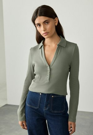 Long-sleeve, olive green top with a collar, V-neck, and five button placket. Paired with high-waisted dark denim jeans. Smooth texture.