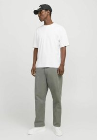Witte katoenen T-shirt gecombineerd met losse grijze broek en witte sneakers. Het model draagt een zwarte pet met een logo-accent.