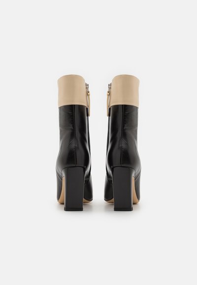 Black leather ankle boots with a beige cuff, square block heels, and a side zipper detail. Smooth texture and minimalist design.