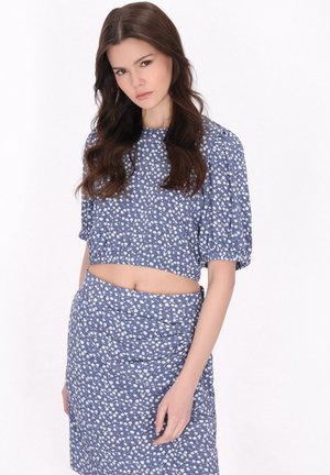 Blå blomster crop top og matchende nederdel med hvide blomstermønstre, som har puffærmer og en tekstureret stoffdesign.