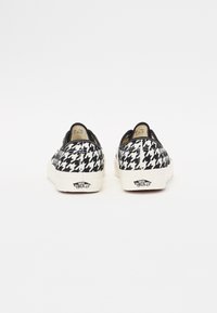Mustavalkoiset houndstooth-kuosiset slip-on-tennarit, joissa on tekstiilistä valmistettu päällinen, valkoinen kumipohja ja merkkilogo kantapäällä. Liukas pinta ja matala profiilimuotoilu.