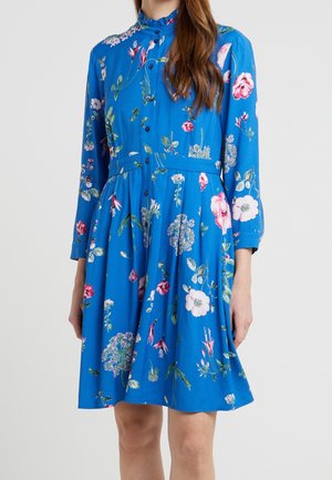 Blauwe jurk tot op de knie met lange mouwen, knoopsluiting aan de voorkant en een meerkleurige bloemenprint, gedragen door een persoon.