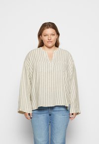 Camisola listrada em creme e bege, apresenta um decote em V, dois bolsos no peito e mangas largas. Tecido suave com um corte relaxado.
