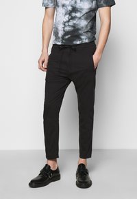 Pantalons noirs ajustés avec une taille élastique et des poches latérales, associés à un t-shirt gris tie-dye et des chaussures noires à boucles.