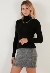 Maglione nero a coste con collo alto abbinato a una mini gonna grigia con texture, impreziosito da una collana in argento come dettaglio accentuante.