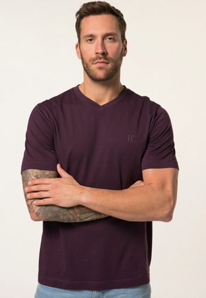 Lila V-Ausschnitt T-Shirt aus weichem Stoff, mit kurzen Ärmeln und einem dezenten Logo auf der Brust. Kombiniert mit hellblauen Jeans.