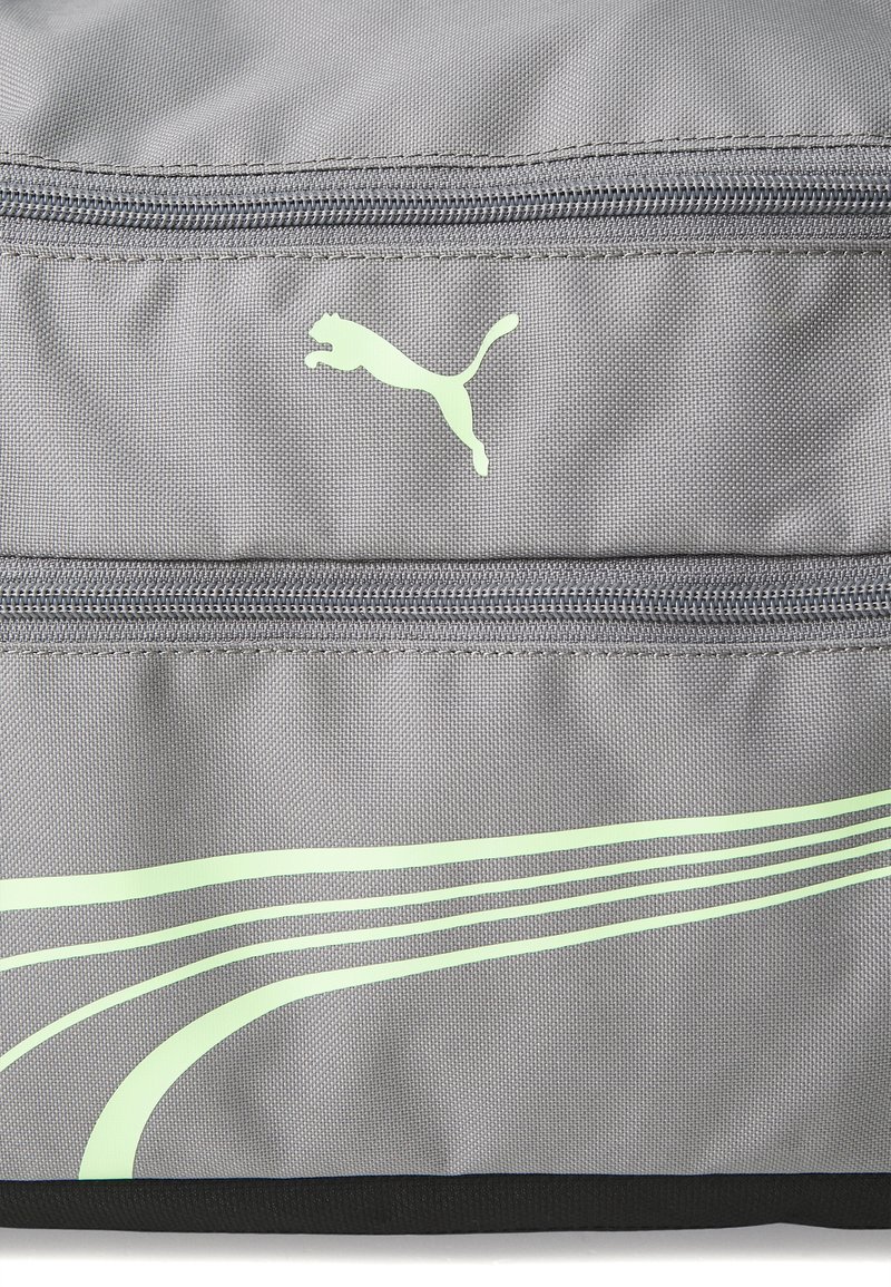 Sac en tissu gris avec une poche zippée, surface texturée, accents noirs et un logo Puma vert avec des bandes courbées vertes sur le devant.