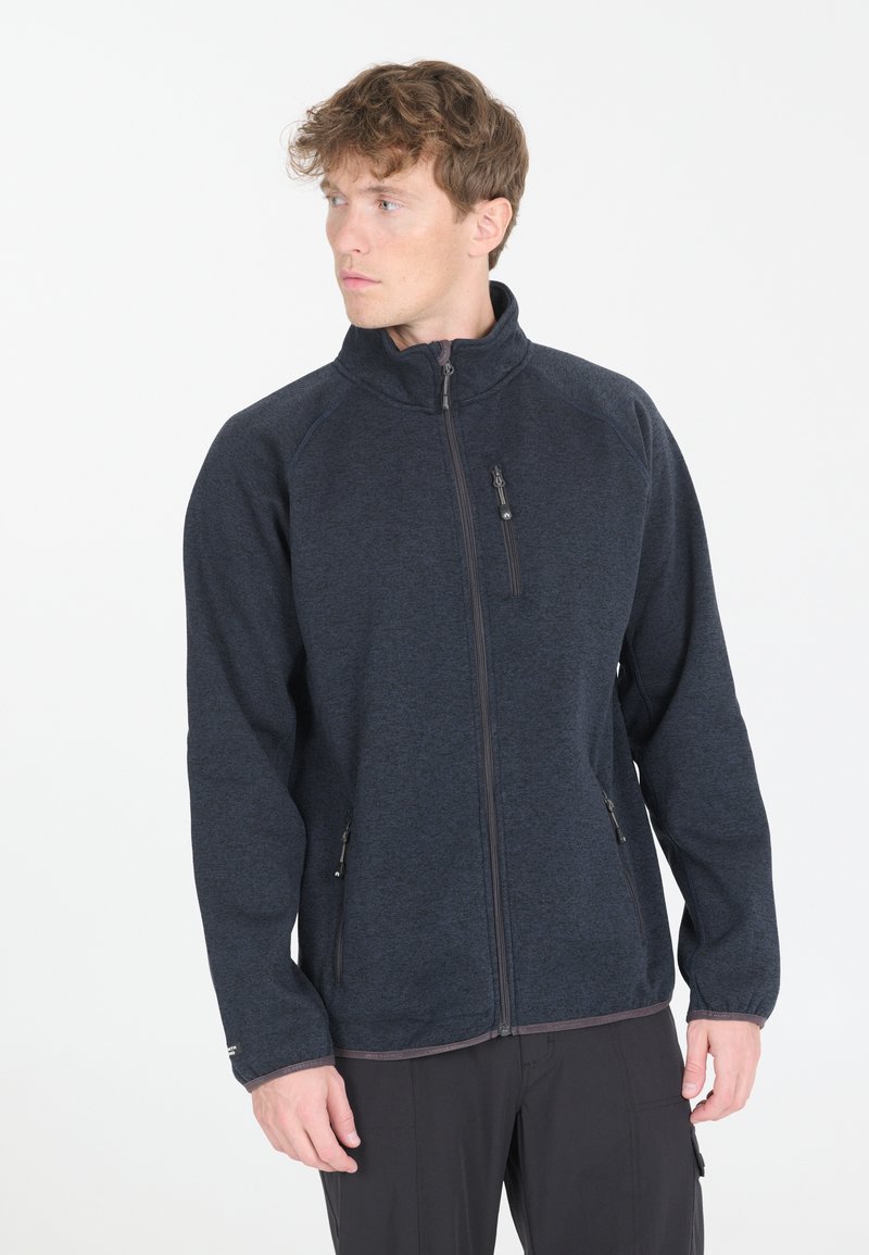 Tummansininen fleece-takki korkealla kauluksella, täysipitkällä vetoketjulla ja kahdella vetoketjullisella sivutaskulla. Takissa on sileä pinta ja joustavat hihansuut.