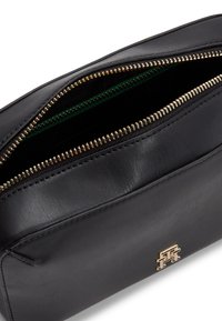 Musta nahkabagi, jossa on kultaiset vetoketjuaukot, vihreä sisävuoraus ja kultainen logovihje etuosassa. Sujuva pinta, suorakulmainen muoto.