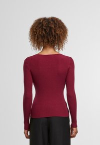 Burgundský žebrovaný pletený svetr s dlouhými rukávy, kulatým výstřihem a přiléhavým střihem, s texturovaným povrchem.