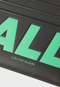 Portofel din piele neagră cu litere îndrăznețe de culoare verde mentă. Designul subliniază marca "Calvin Klein" și are o finisare texturată.