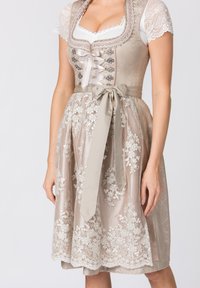 Traditionelles Dirndl in sanftem Beige mit floralem Spitzenmuster, Satinschnürung und einer taillierten Korsage. Eleganter Rock mit aufwendiger Stickerei.