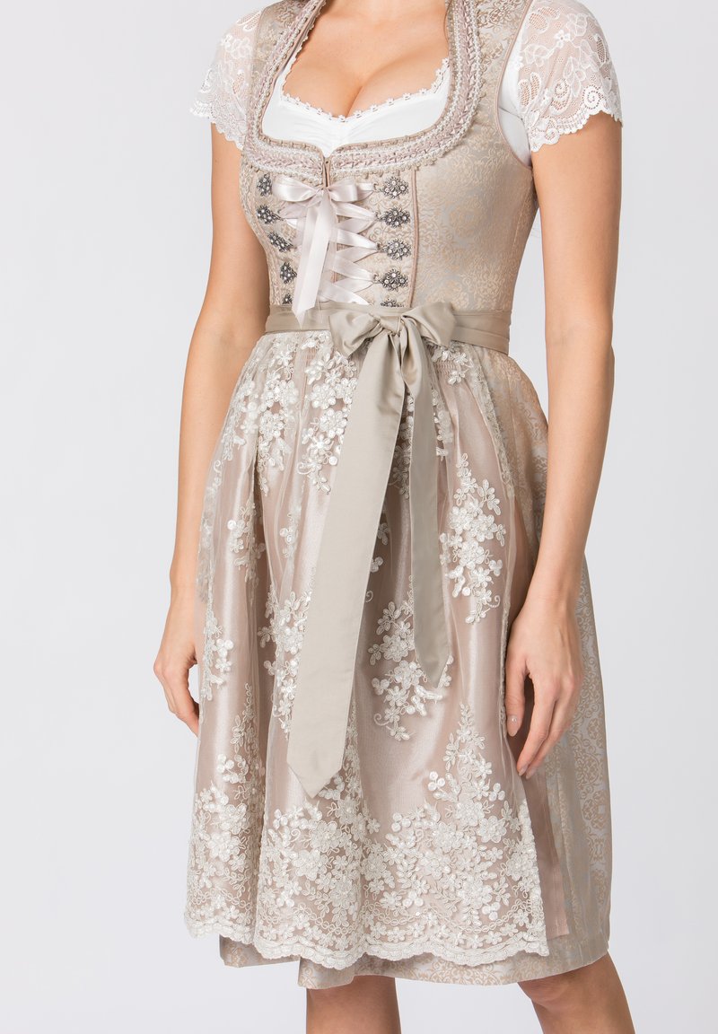 Traditionelles Dirndl in sanftem Beige mit floralem Spitzenmuster, Satinschnürung und einer taillierten Korsage. Eleganter Rock mit aufwendiger Stickerei.