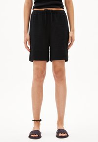 Black waffle-textured shorts with an elastic waistband and drawstring. Smooth trim and knee-length cut. Paired with flat slide sandals.