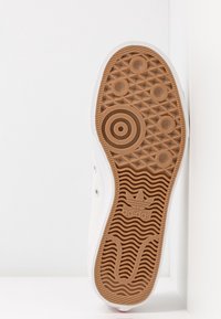 Sula av en Adidas-sneaker med brun strukturerad gummi, cirkulära mönster, vågiga linjer och Adidas trefoil-logotyp i mitten.