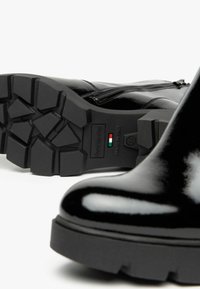 Bottines en cuir verni noir avec une semelle épaisse en caoutchouc texturé, dotées d'une fermeture éclair et d'un logo en relief sur la semelle.