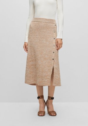Beige strikket midi nederdel med knapdetaljer i siden, brugt med hvid top med lange ærmer og brune hælede sandaler.