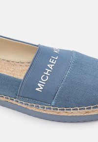 Espadrille en toile bleue avec semelle en jute tressé et caoutchouc, avec le texte blanc "MICHAEL KORS" sur la bride supérieure.