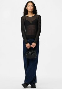 Sort gennemsigtig bluse med lange ærmer, prydet med polka prikket mønster og bølgede kanter, parret med høj talje mørk denim bukser med bred ben og en lille sort taske.