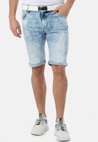 Hellblaue Denim-Shorts mit umgeschlagenen Säumen, Fünf-Taschen-Design und einem weißen Gürtel. Sneakers mit blauen Akzenten und reflektierenden Schnürsenkeln.