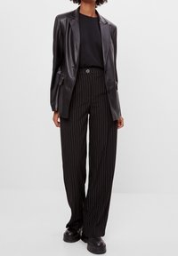 Svart läderblazer över en svart t-shirt, kombinerad med högmidjade svartvita randiga vida byxor och kraftiga svarta skor.