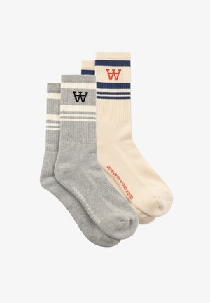 Twee paar ribgebreide sneakersokken, één beige met blauwe strepen en een rode "W"-logo, één grijs met witte strepen en een zwart "W"-logo, naast elkaar gevouwen.