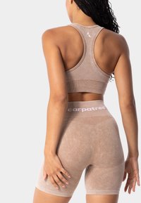 Brūns sporta krūšturis un atbilstošas šortus, kas izgatavoti no mīksta, teksturēta materiāla. Krūšturim ir sacensību muguras dizains, ar logotipa akcentiem uz joslas.